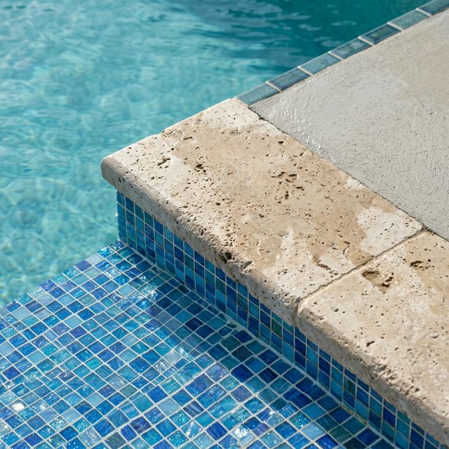 Détail de mosaïque bleue et margelle en pierre naturelle sur une piscine béton